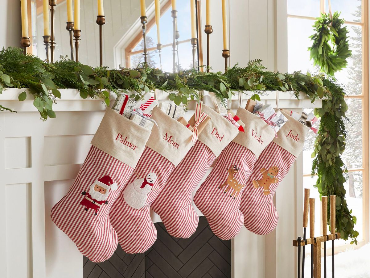 five Gingerbread Ticking Stripe Christmas Stockings hanging on a white wooden fireplace mantle decorated with green garland
