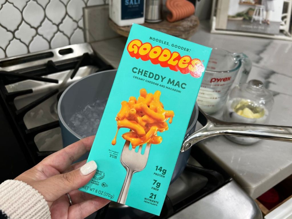 hand holding box of Goodles Mac & Cheese in front of stove