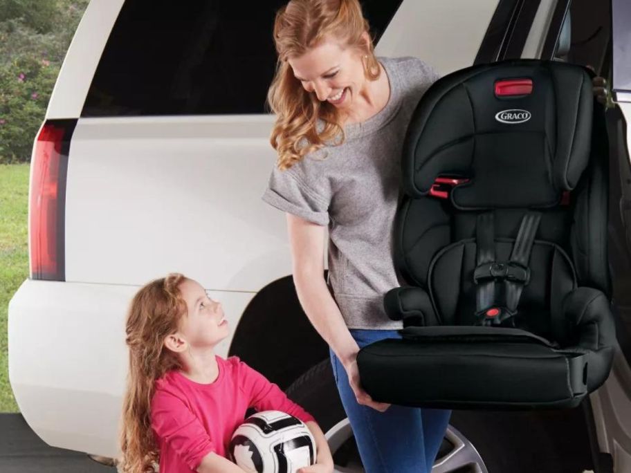 woman holding Graco Tranzitions 3-in-1 Harness Booster Car Seat next to car