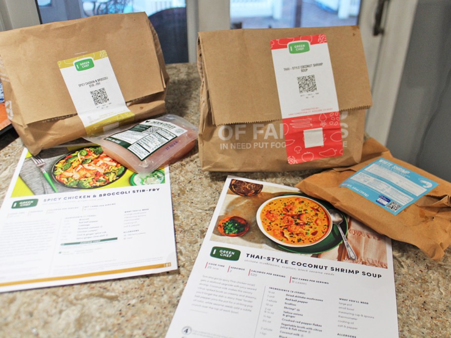 two green chef bags, packages of meats, and recipes cards on kitchen counter