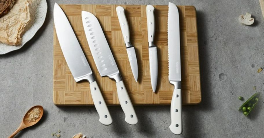 different sizes of Carote stainless steel knives with white handles shown laying on a wood cutting board