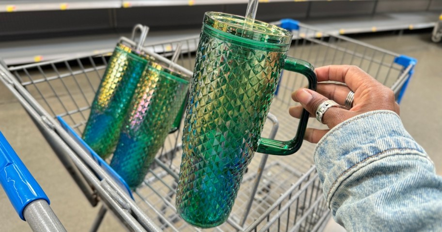 hand holding a green and blue studded iridescent large tumbler with handle with a walmart cart in the background with more in cart