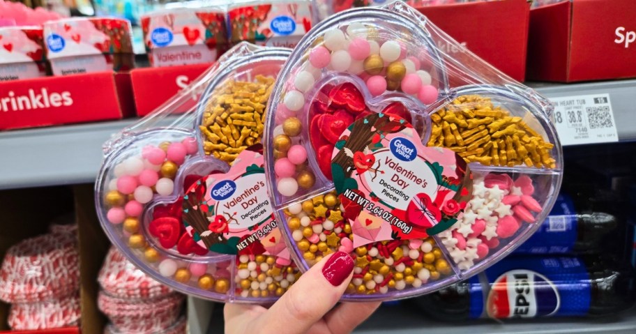 hand holding up two plastic heart shaped containers with Valentine's themed sprinkles and decorations for baking