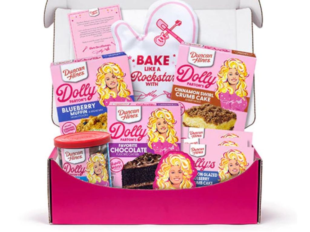 pink box filled with various Dolly Parton baking items, cake mixes, oven mitt, frostings