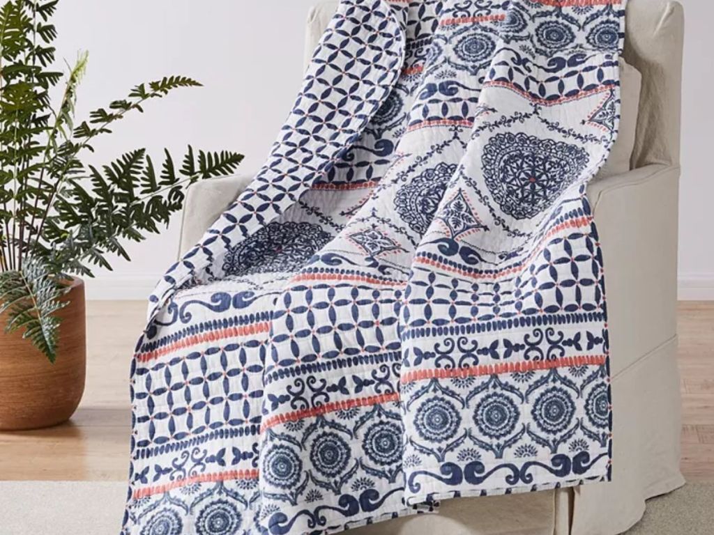 colorful blue, orange and white patterned reversible quilted throw over a chair with a plant beside it