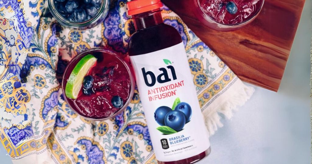 bottle of Bai blueberry drink beside a glass full of the drink on a colorful kitchen towel
