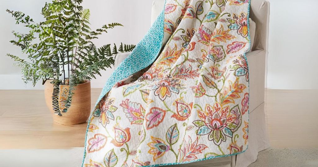 colorful cream, orange, teal, pink, boho floral patterned reversible quilted throw over a chair with a plant beside it