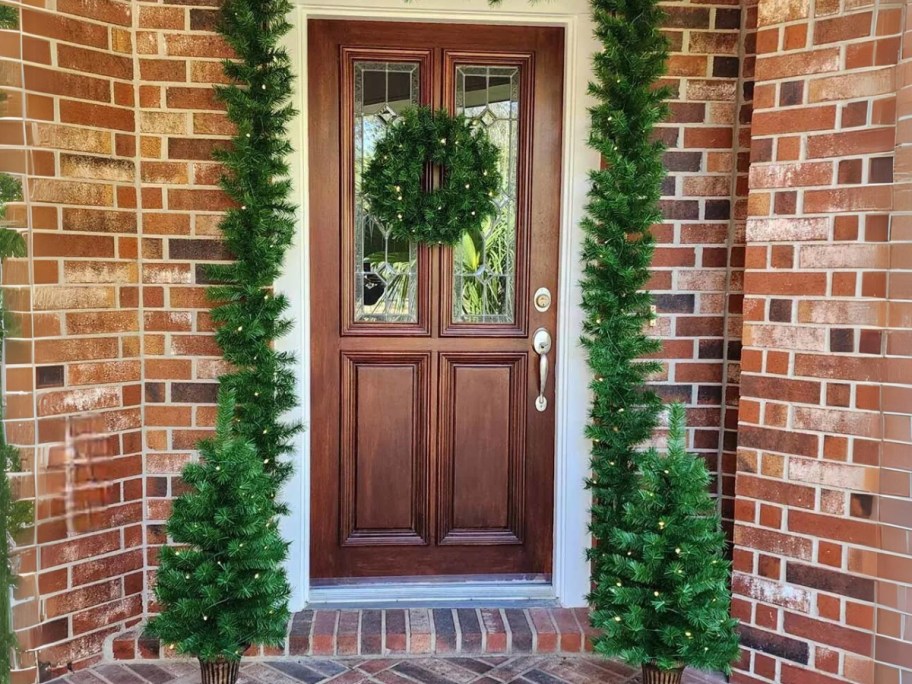 a front porch with matching Christmas decor set with garland, wreath and faux trees in pots