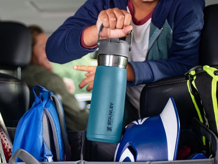 little boy reaching to the back of an SUV holding a teal and grey Stanley water bottle with a handle
