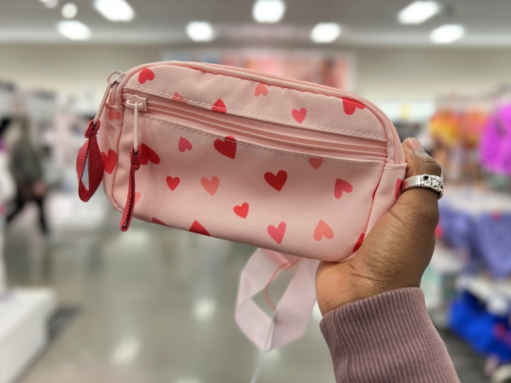 Hand holding pink heart fanny pack at a store