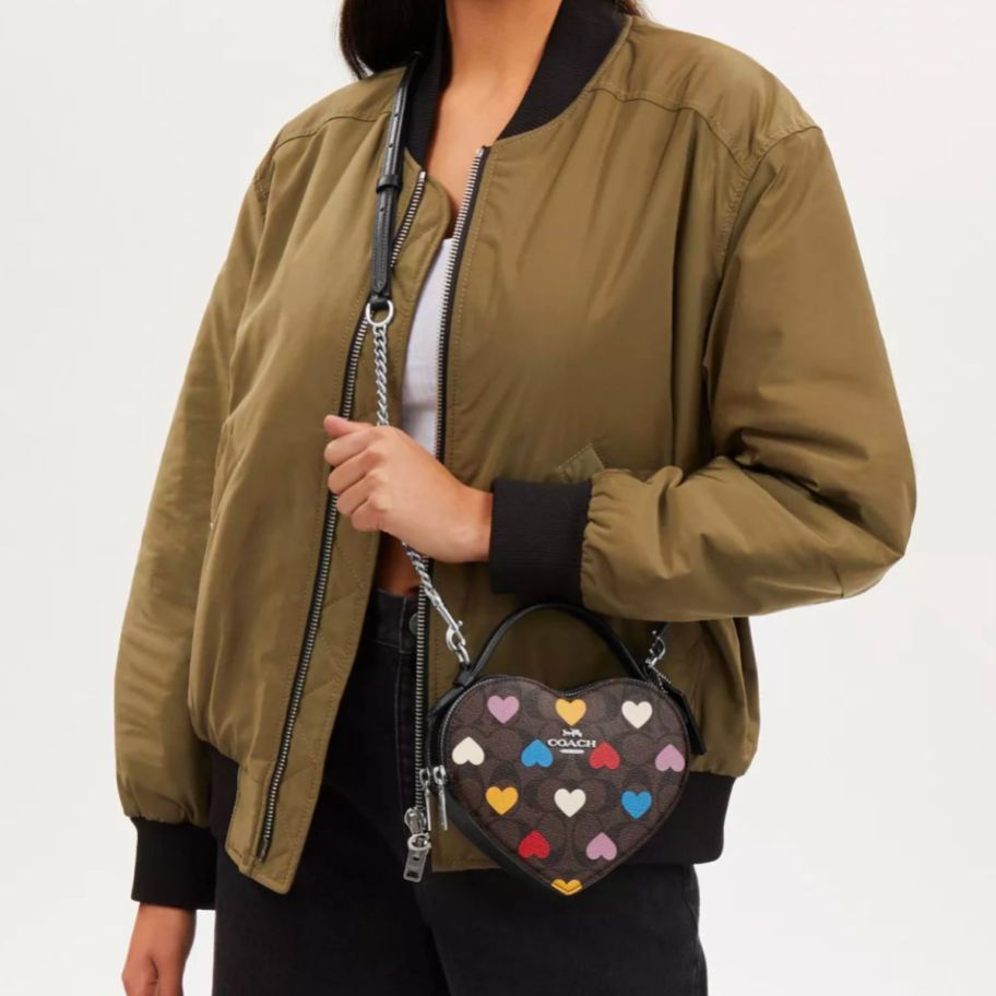 a model wearing a coach heart shaped crossbody purse in white with pink and brown signature canvas