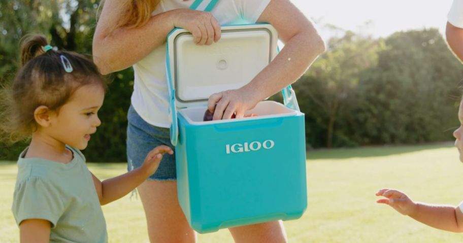 woman opening a turquoise blue Igoo personal cooler and pulling snacks out for a kid