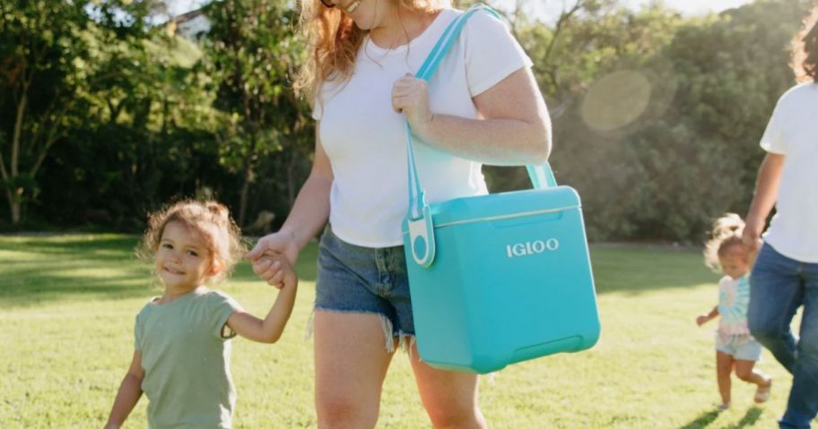 woman carrying a turquoise blue Igloo personal cooler with a carry strap walking with a child 