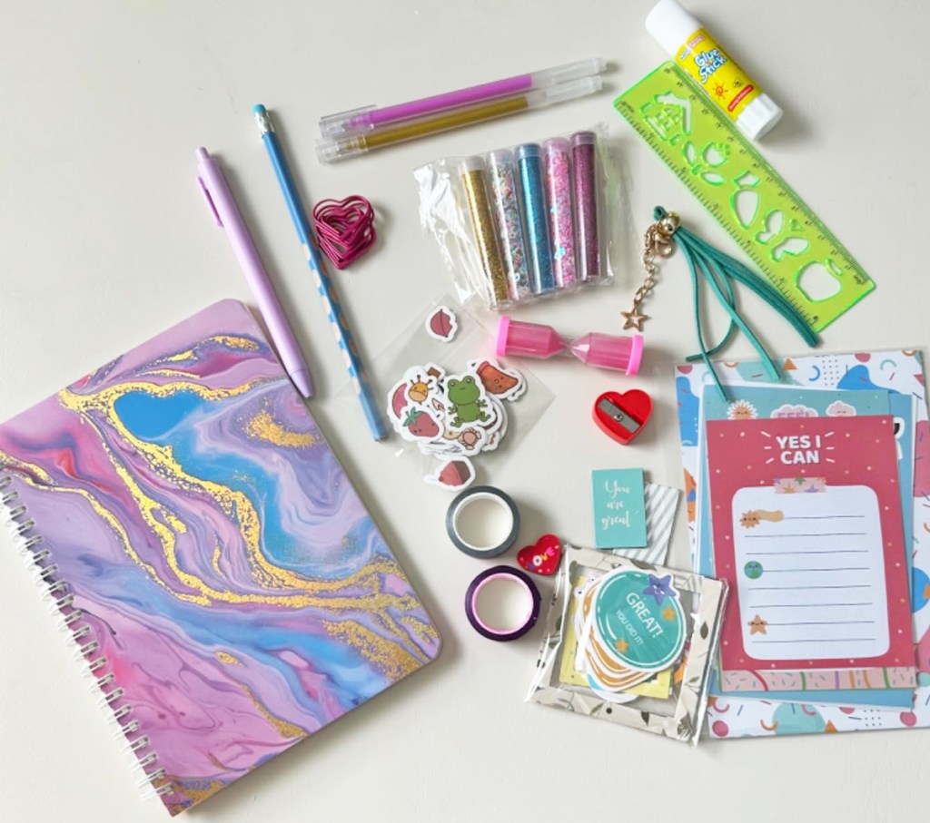 marble print journal with glitter, pens, stickers, and more supplies near it