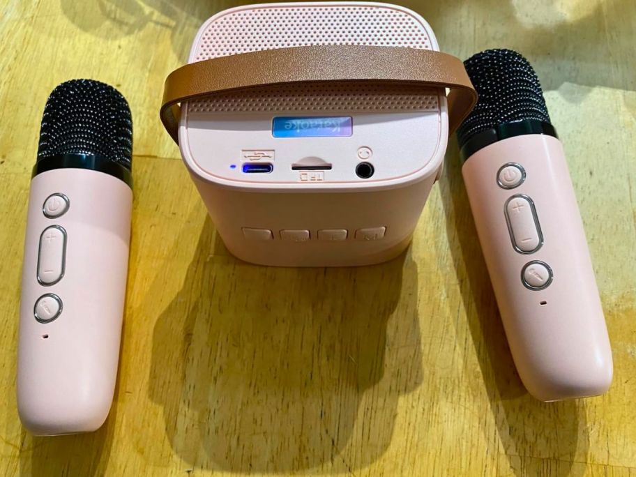 light pink mini karaoke machine speaker with 2 mics sitting on counter