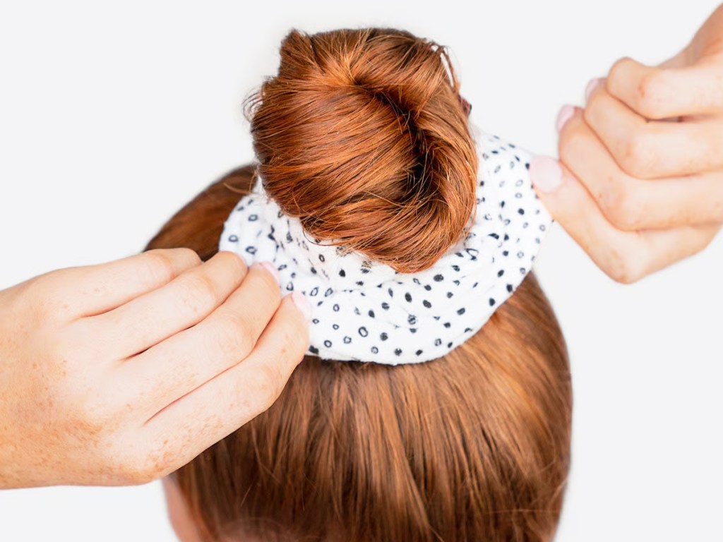 woman with red hair putting hair into a bun with scrunchie
