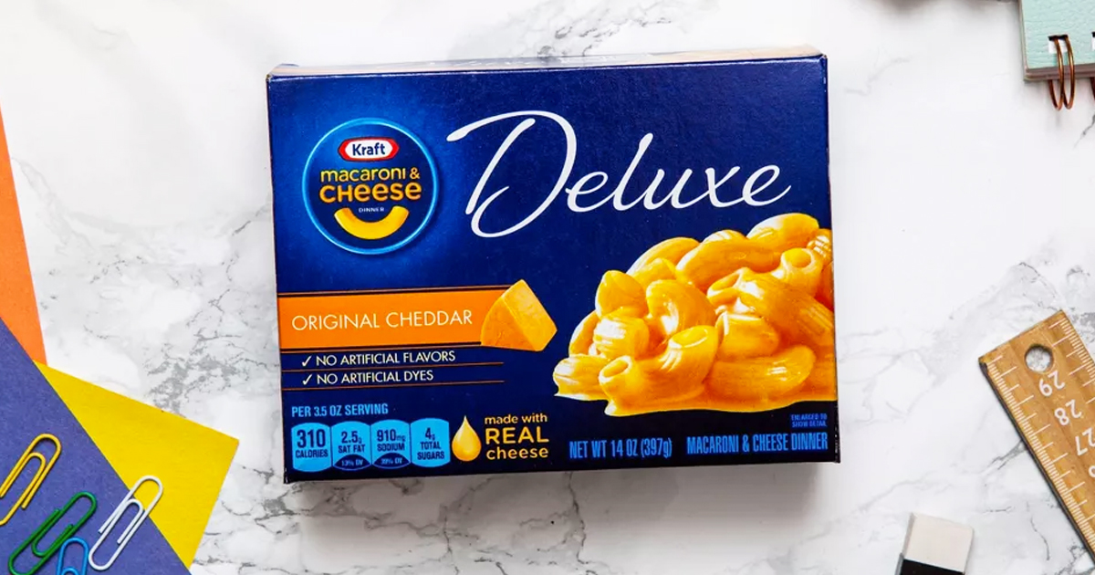 blue box of Kraft Deluxe Original Cheddar Macaroni & Cheese Dinner on table with school supplies
