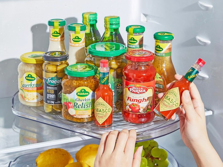 person spinning lazy susan in fridge with condiments and jars on it