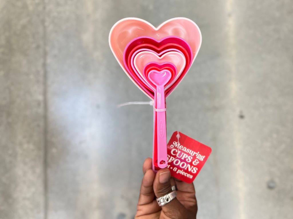 a womans hand holding a set of pink and read heart shaped Measuring cups and spoons set