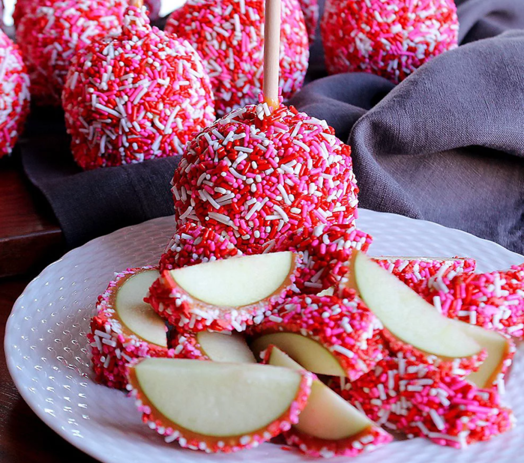 Several Mrs. Prindables Caramel Apples covered in pink sprinkles which is one of the best food basket gifts for Valentine's Day 2024