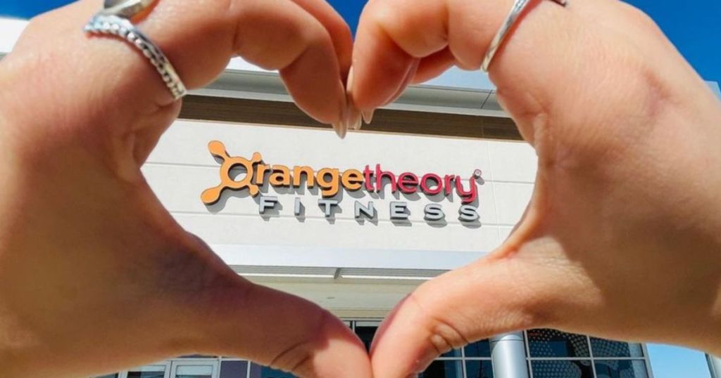 Hands making a heart around the sign on an Orange Theory Fitness Gym