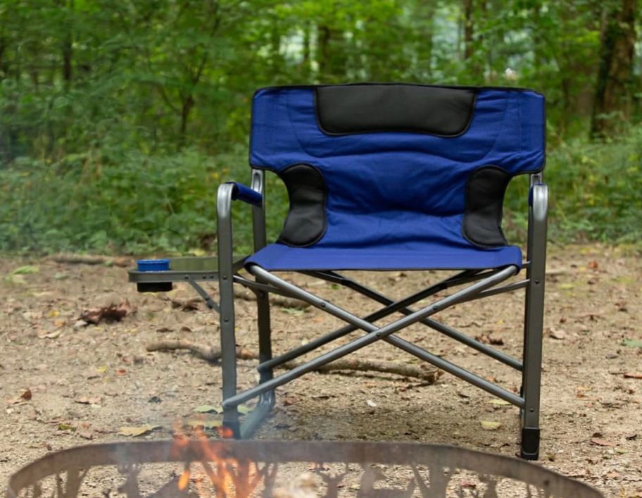 a blue camping chair with side table sitting next to campfire