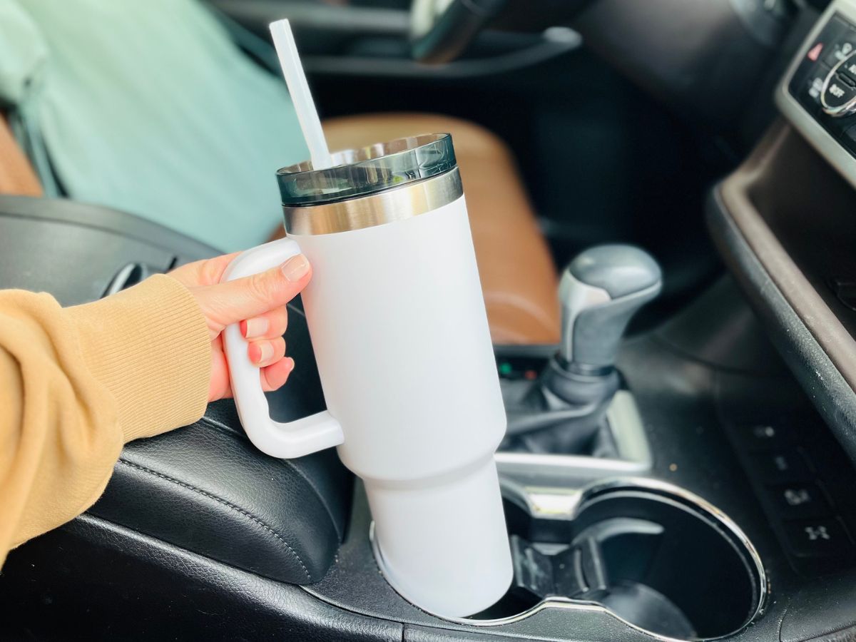 An Ozark Trail 40oz Tumbler in the car being placed in the cupholder in the center console