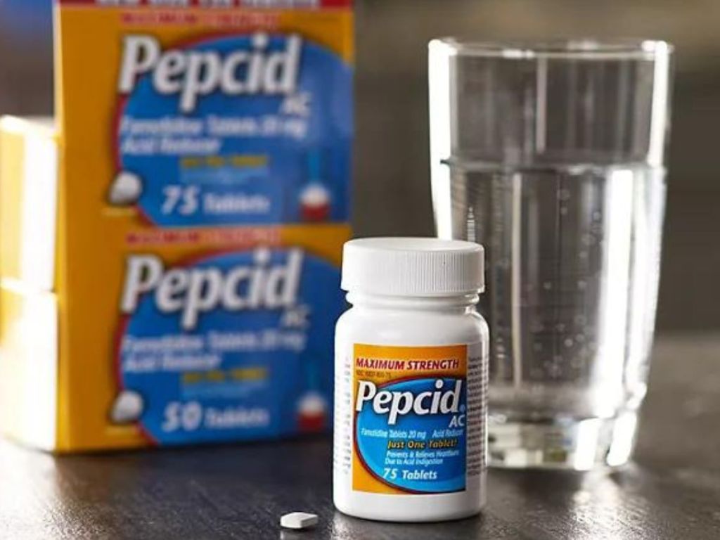 A bottle of Pepcid AC next to a whole box and a glass of water