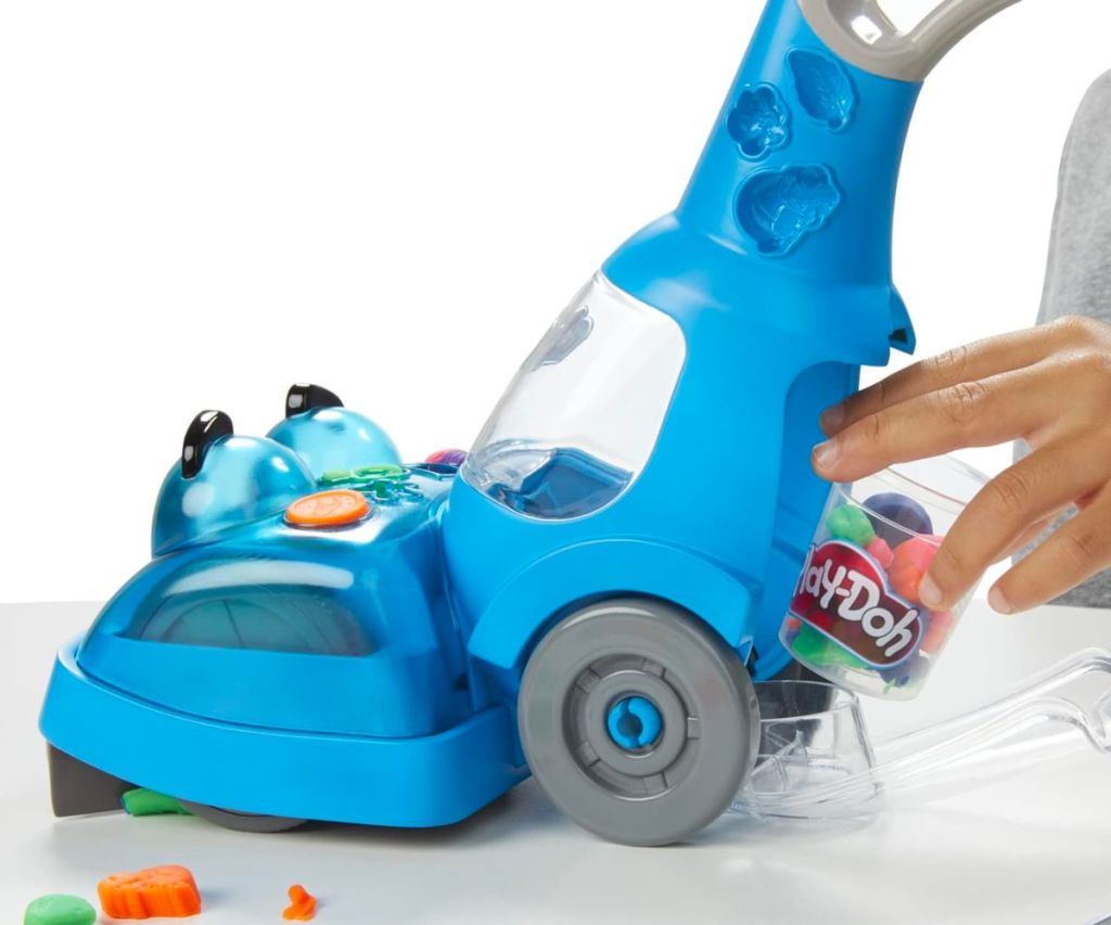 side view of small blue plastic play vacuum with a kids hand removing the dust bin 