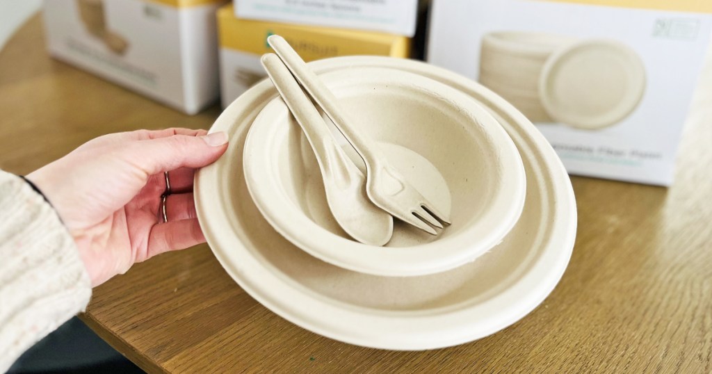 woman's hand holding up a set of disposable utensils, bowl, and plate