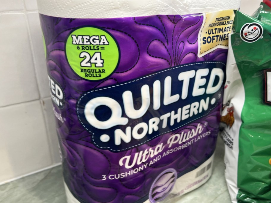 purple package of quilted norther toilet paper on kitchen counter near bag of chips