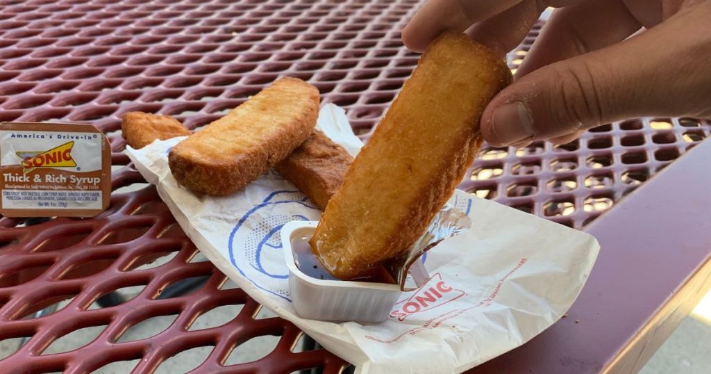 Hand dipping a sonic french toast stick in syrup