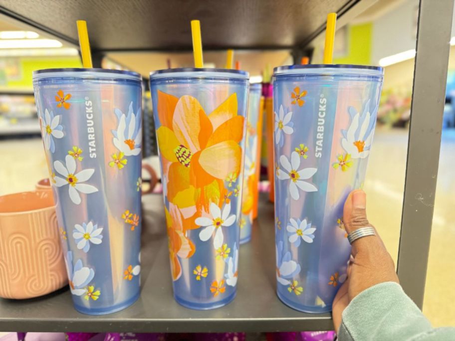 hand reaching for a Starbucks cold cup that is blue with daisies and yellow and orange flowers