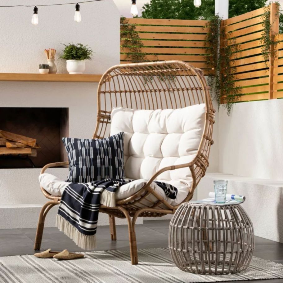 a double wicker egg chair next to an outdoor fireplace on a patio