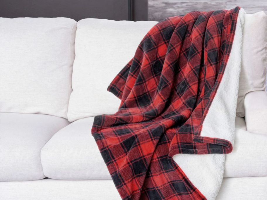 a red and black buffalo plaid heated blanket draped over the back corner of a white sofa