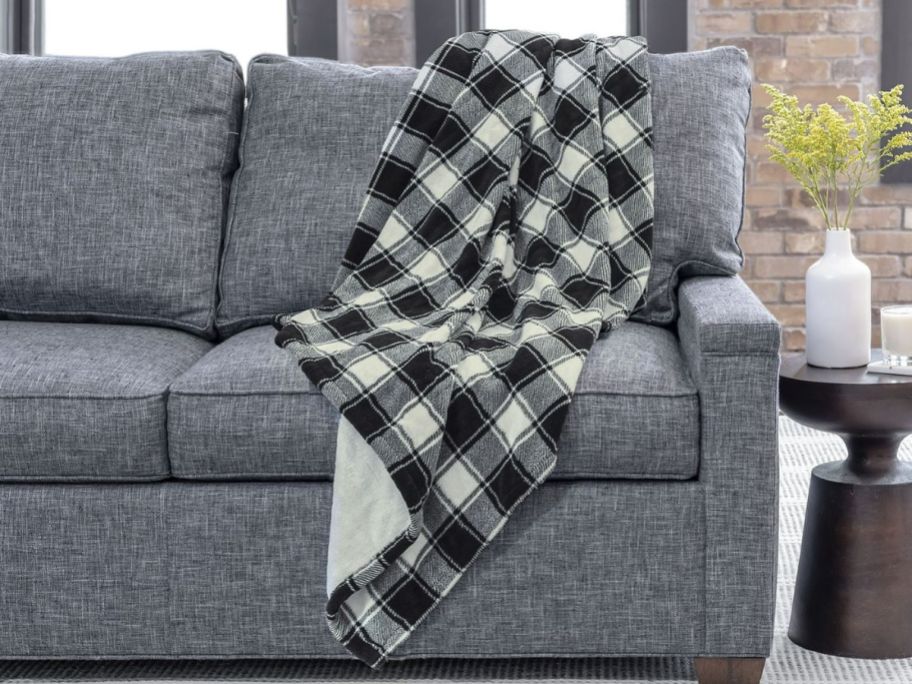 a white and black buffalo plaid heated blanket draped over the back corner of a gray sofa