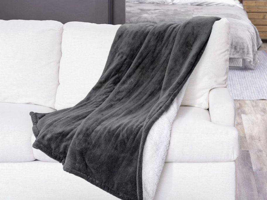 a slate gray heated thrw blanket draped over the back corner of a white sofa