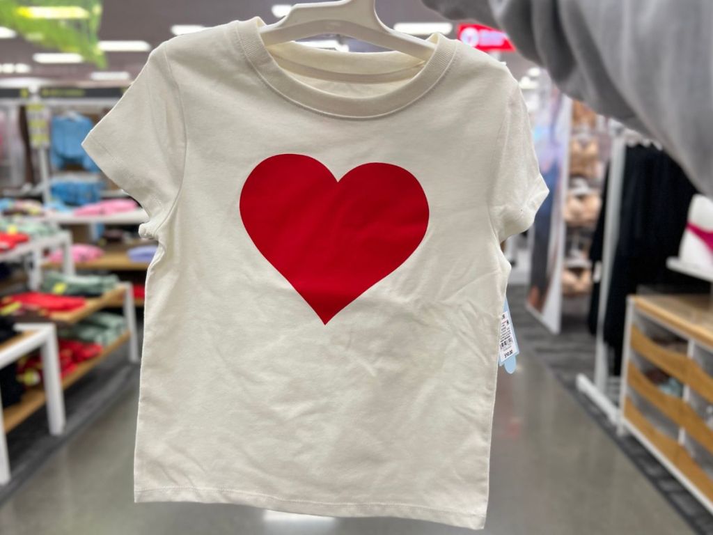 hand holding an off white toddler t-shirt with a red heart on it