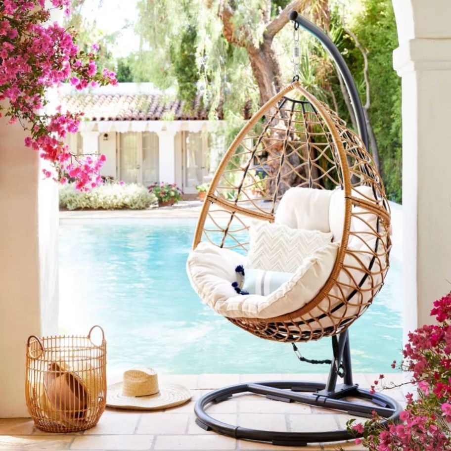a hanging egg chair with white cushions next to a pool