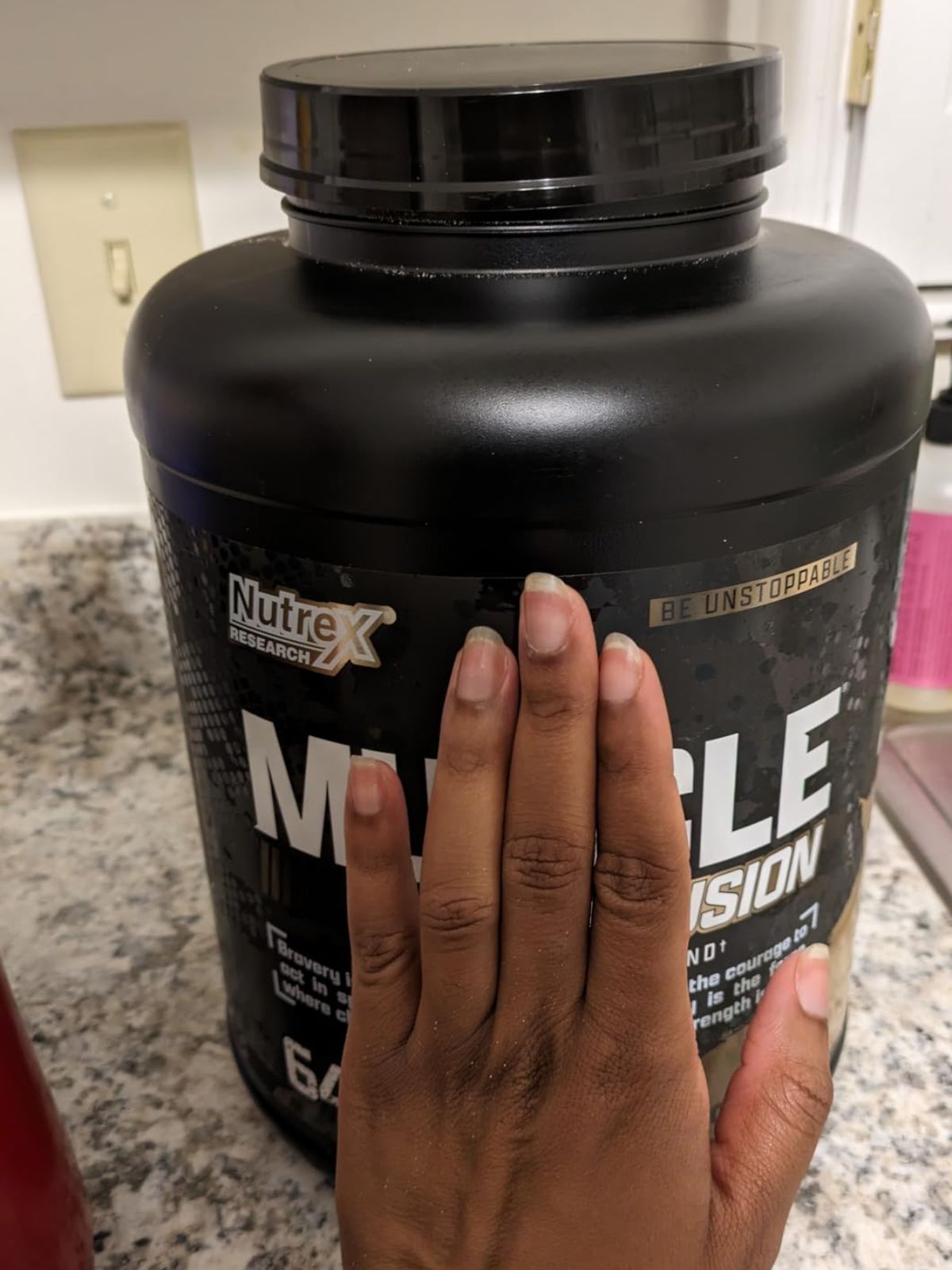 woman holding her hand up to a Nutrex Research Muscle Infusion Advanced Whey Protein Blend Powder to show how big the container is
