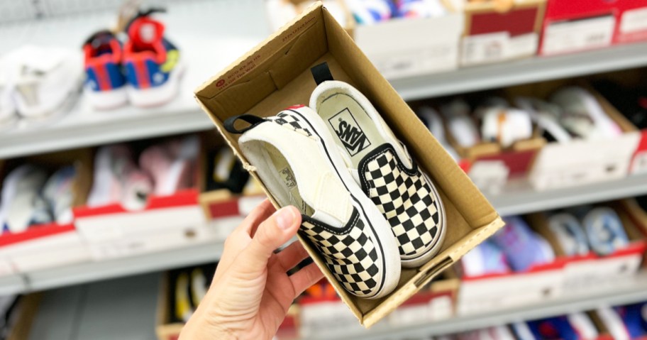 hand holding up a pair of black and white checkered vans sneakers in shoe box