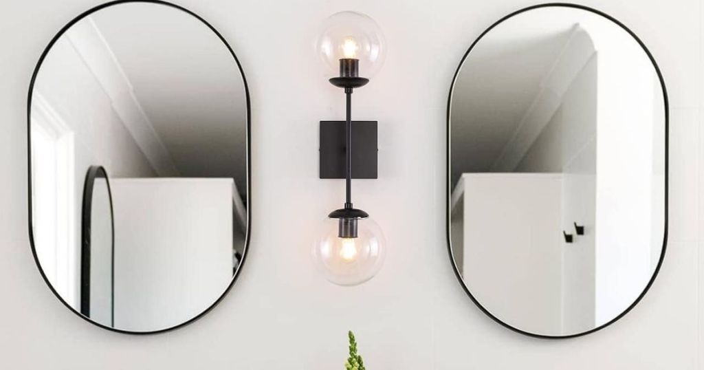 A bathroom with a glass sconce light between 2 mirrors