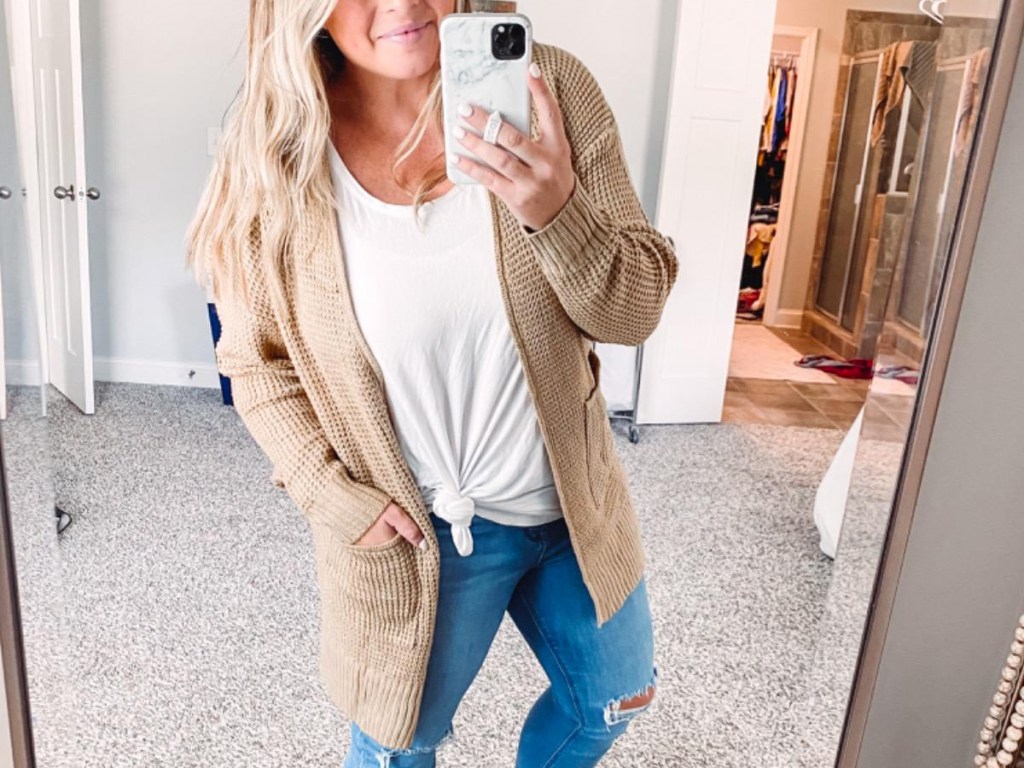 woman taking photo in mirror wearing tan cardigan over white tee and jeans
