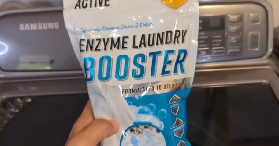 hand holding a Active Enzyme Laundry Booster Odor Remover bag in front of a washing machine