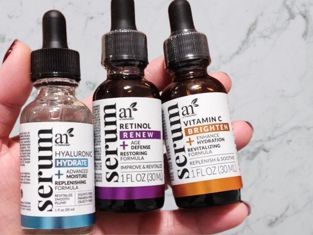hand holding three artnaturals serum from anti-aging set over marble counter
