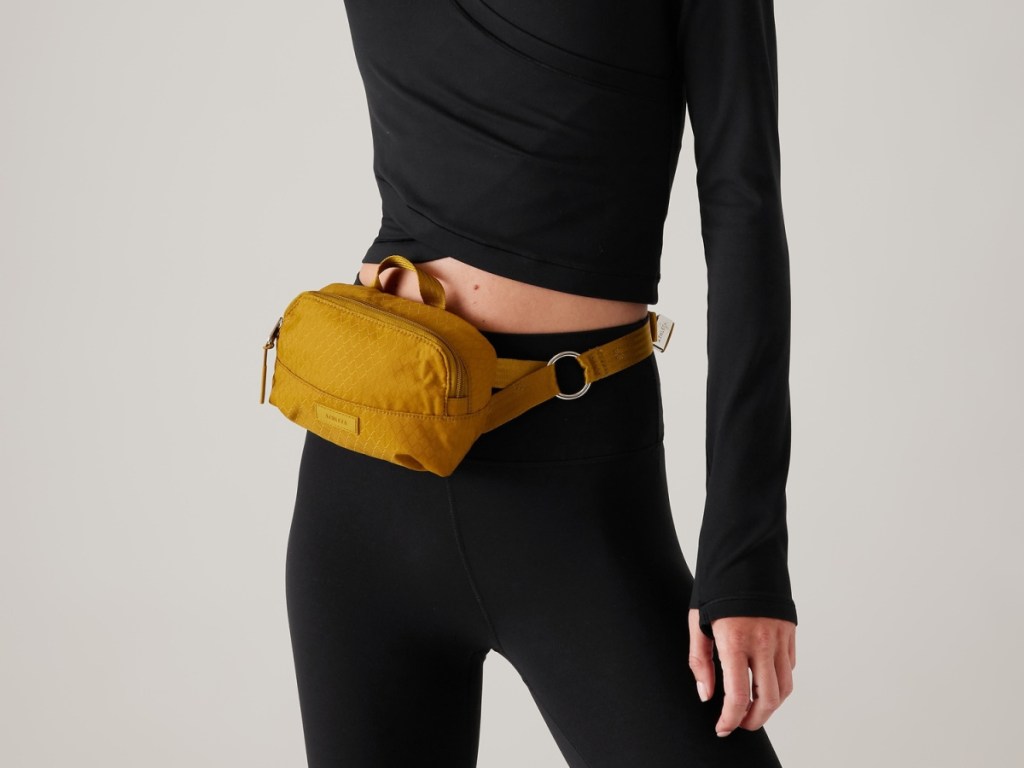 woman wearing a black top and pants and a tan athleta belt bag