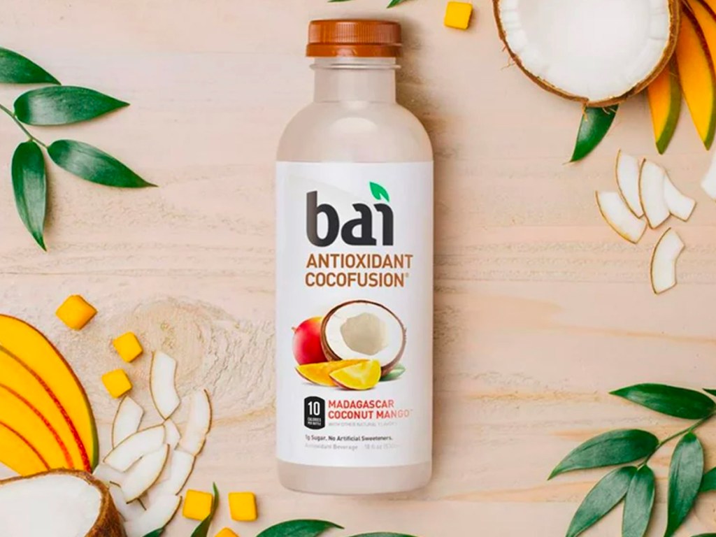 bai coconut mango bottle on table next to nuts, mangos, and leaves