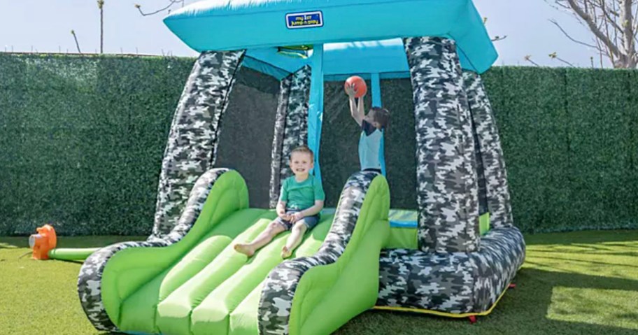 blue and green inflatable bounce house with kid playing basketball and one sliding 