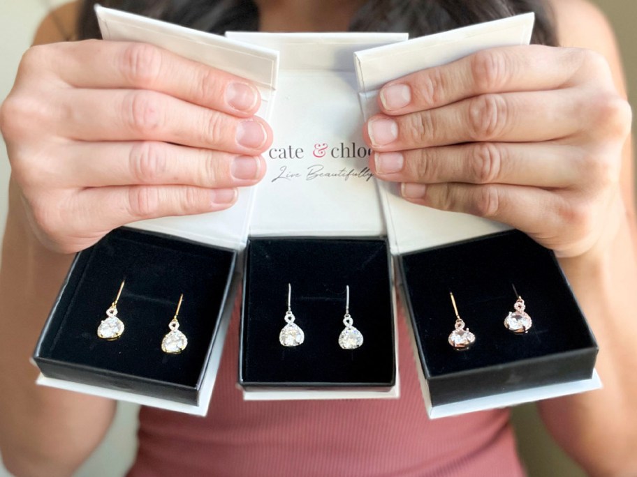 hands holding three cate and chloe drop earrings boxes 