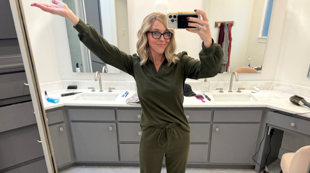woman holding up arms in dark green lounge set standing in bathroom